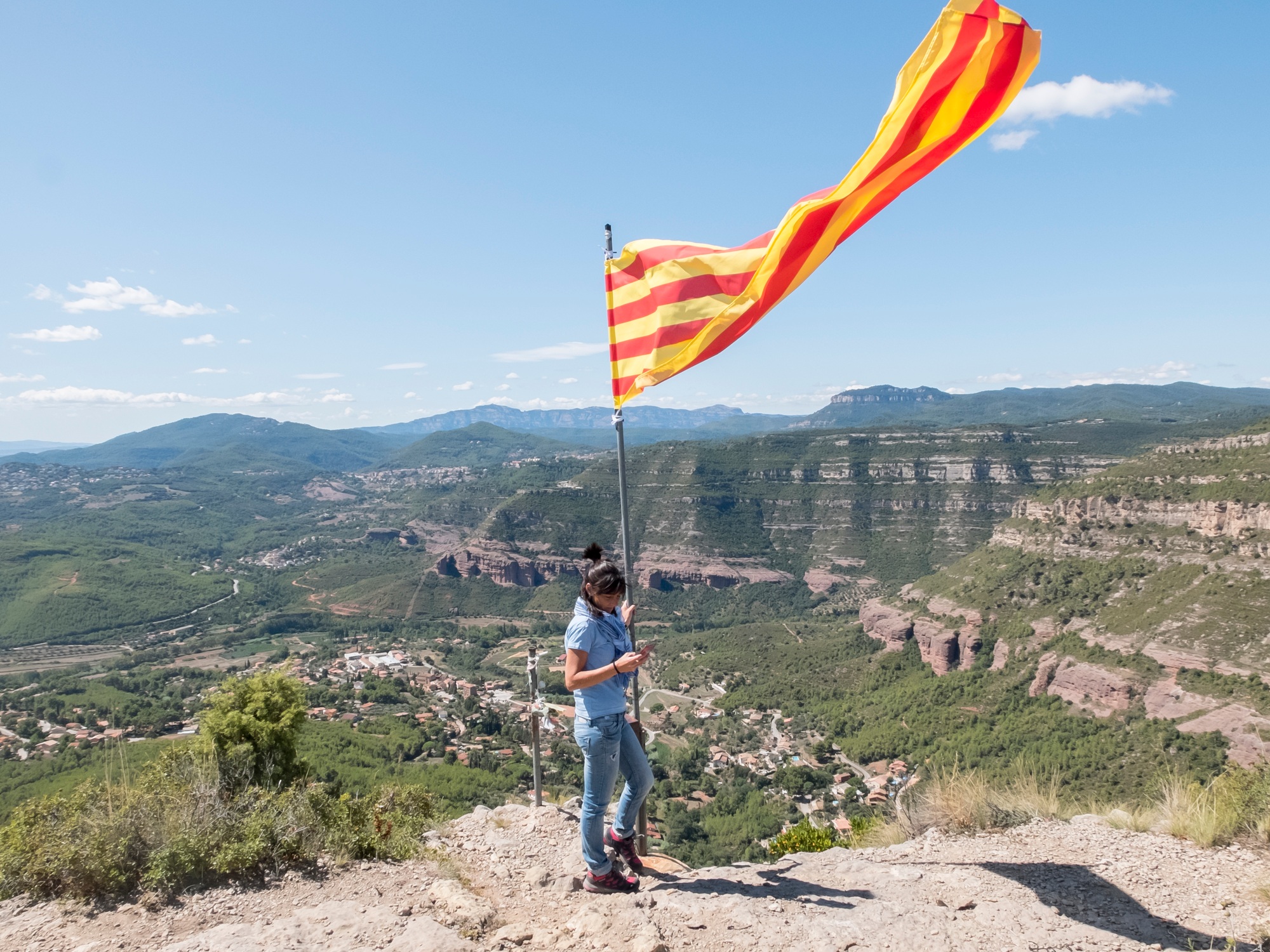Une femme tenant un drapeau catalan au sommet d'une montagne tout en utilisant son téléphone portable.